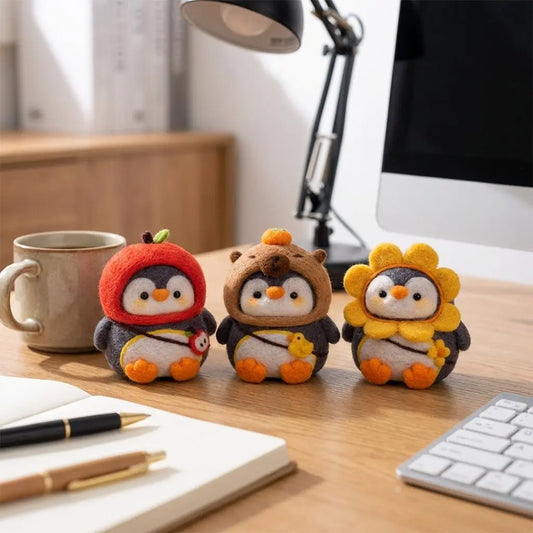 Three needle felted penguins in sunflower, capybara and apple hoodies on a desk