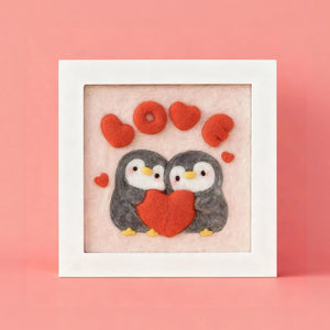 Finished Penguin Love wool felt frame with two penguins holding a red heart, made from the Joypok beginner needle felting kit